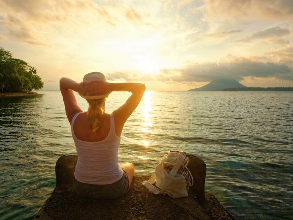 Rear view of a romantic young woman sitting on the pier enjoying stunning sunset